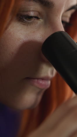 focused woman with red hair looks through electronic microscope on blurred background. young female person examines rare type of bacteria in laboratory closeup