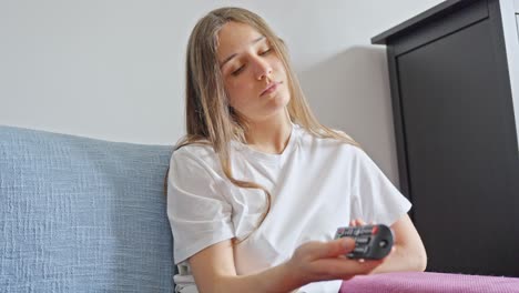mujer inclinada y aburrida en el sofá mientras presiona los botones del control remoto hacia la tv en casa, primer plano estático