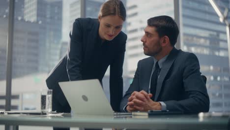 successful corporate ceo and investment manager talking, using laptop computer while sitting in meeting room in office. two successful businesspeople brainstorm on prospective fintech investment deal.