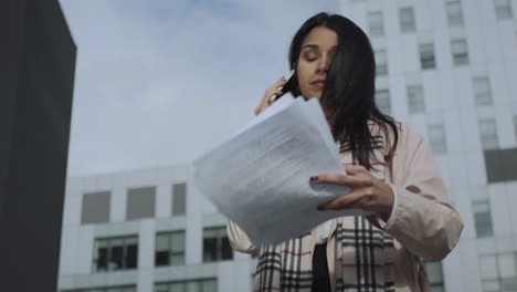 mujer de negocios hablando con un teléfono inteligente en la calle. chica ocupada leyendo documentos al aire libre