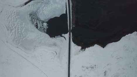 Bird's-eye-view-of-a-car-driving-on-a-bridge-in-Iceland-in-winter