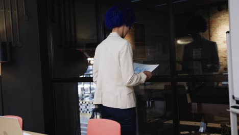 Biracial-casual-businesswoman-with-blue-afro-reading-documents-in-meeting-room,-slow-motion
