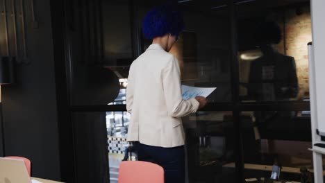 mujer de negocios casual de dos razas con afro azul leyendo documentos en la sala de reuniones, en cámara lenta