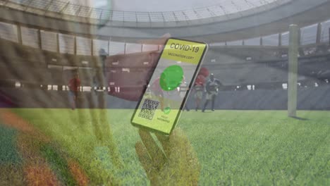 animation of woman holding smartphone with covid 19 vaccination passport over football players