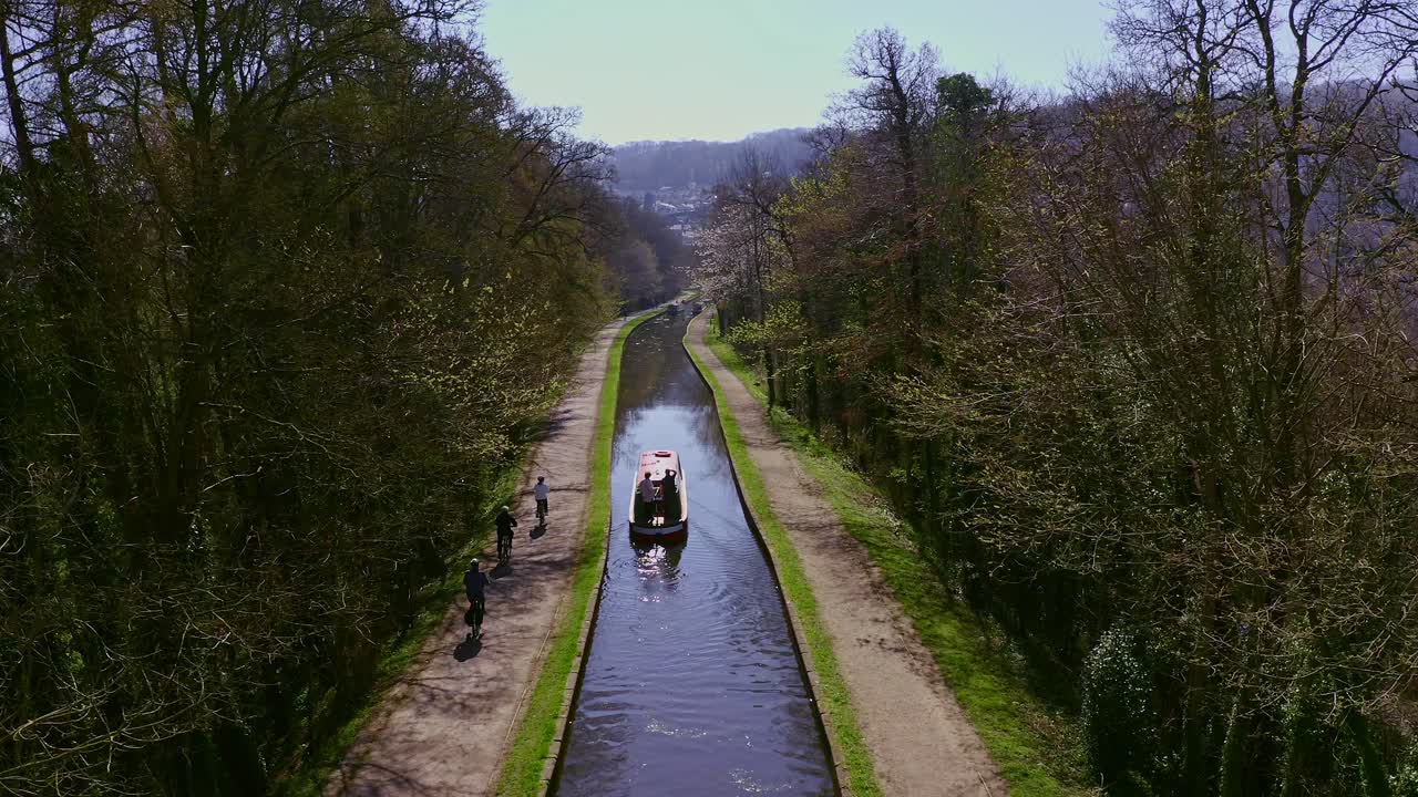 un barco estrecho que se dirige río arriba después de cruzar el acueducto pontcysyllte, diseñado por thomas telford, ubicado en la hermosa campiña galesa, famosa ruta del canal llangollen, mientras los ciclistas pasan