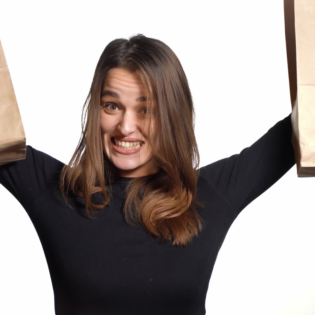 A pretty woman with long hair is holding paper packages in her hands and showing it on a white background in the studio. Shopping