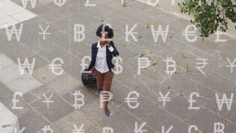 animación de símbolos de moneda sobre una mujer de negocios afroamericana hablando con un teléfono inteligente en la calle