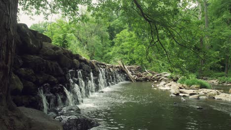 Seitenansicht-Von-Gestapelten-Steinen,-Die-Einen-Damm-Bilden,-Und-Wasser,-Das-In-Den-Bach-Fällt