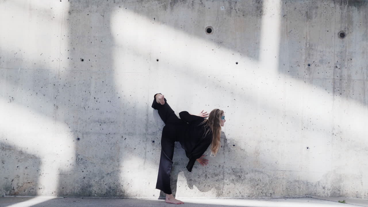Esercizio di danza stile balletto d'ombra davanti a un muro trasandato.
