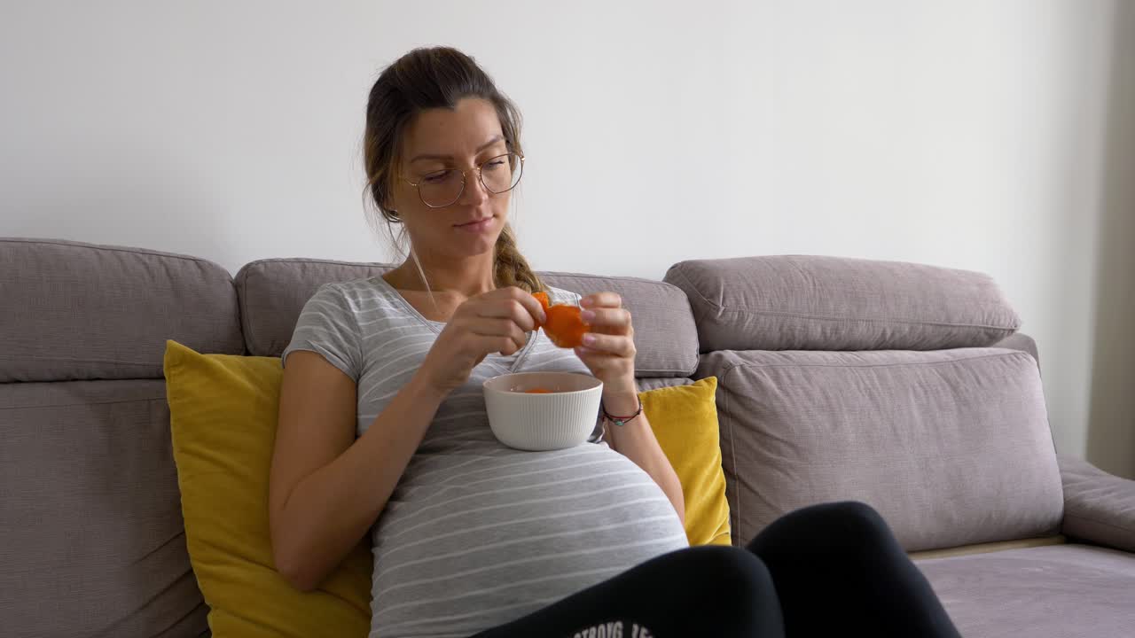 안경을 쓴 아름다운 임산부는 귤 껍질을 벗기고 먹는다