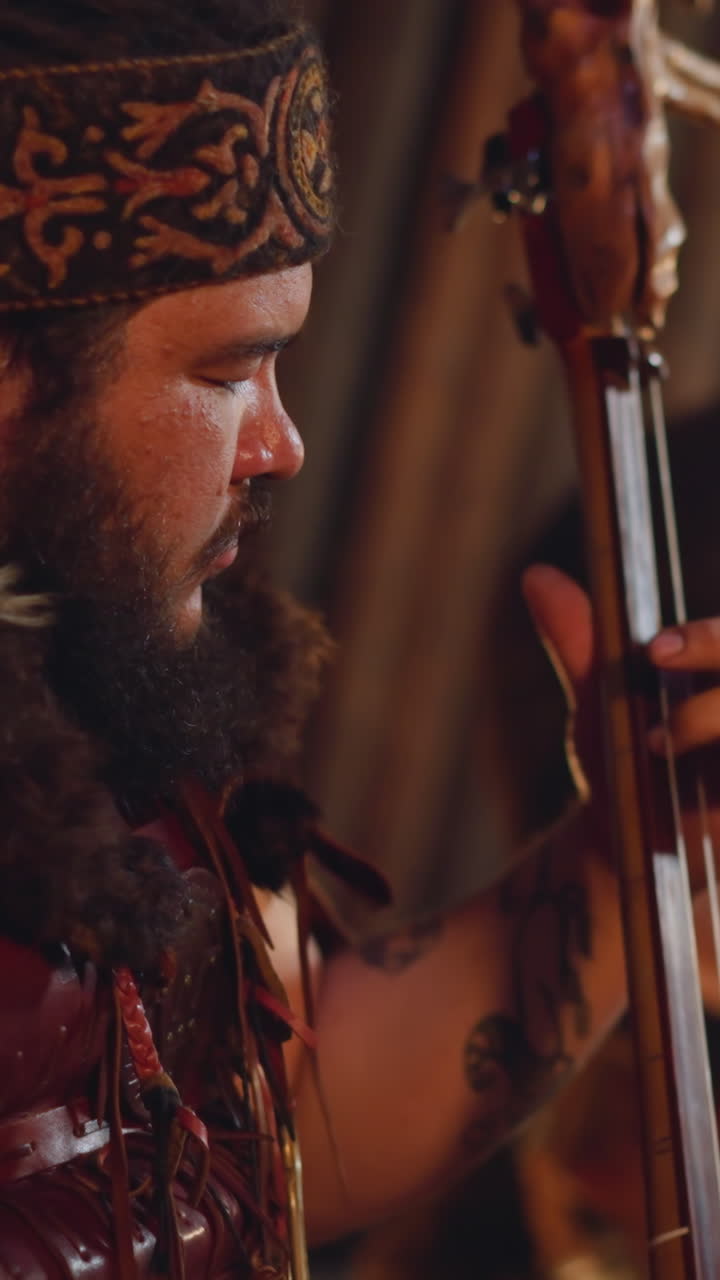 Bearded person plays two-string instrument while colleague taps drum set in traditional entertainment hub closeup. Concert of shamanic Altai music