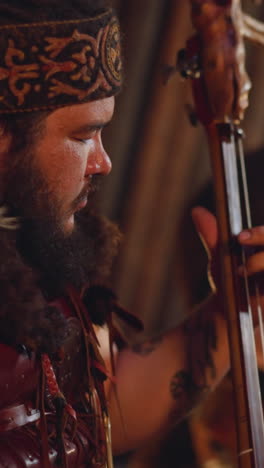 bearded person plays two-string instrument while colleague taps drum set in traditional entertainment hub closeup. concert of shamanic altai music