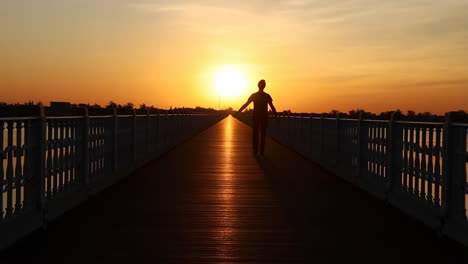 person silhouetted walking on a bridge at sunset