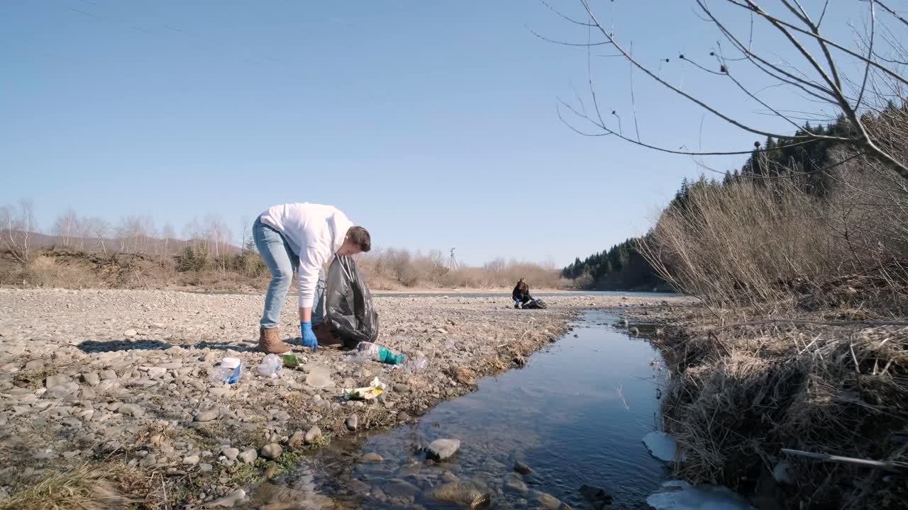 Teamwork cleaning plastic on the beach. Volunteers collect trash in a trash bag. Plastic pollution and environmental problem concept. Voluntary cleaning of nature from plastic. Greening the planet