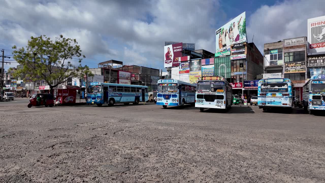 Local buses are parked at the Anuradhapura bus stop in Sri Lanka, showcasing vibrant colors and bustling city life.