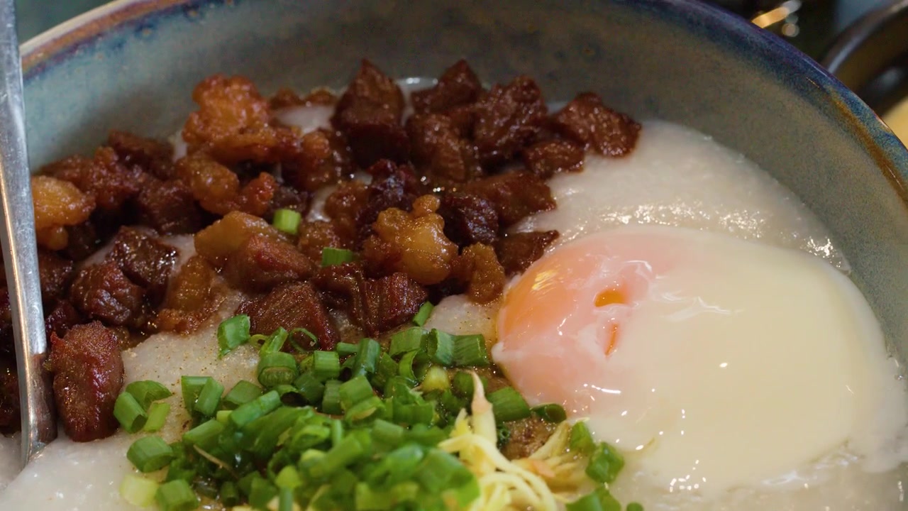 Tampilan dekat bubur gurih dengan taburan jahe, daun bawang, dan abon babi