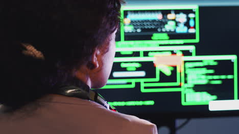 rear view of female teenage hacker sitting in front of computer screens bypassing cyber security