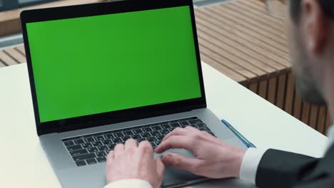 over the shoulder shot of a businessman typing on laptop and looking at green screen.