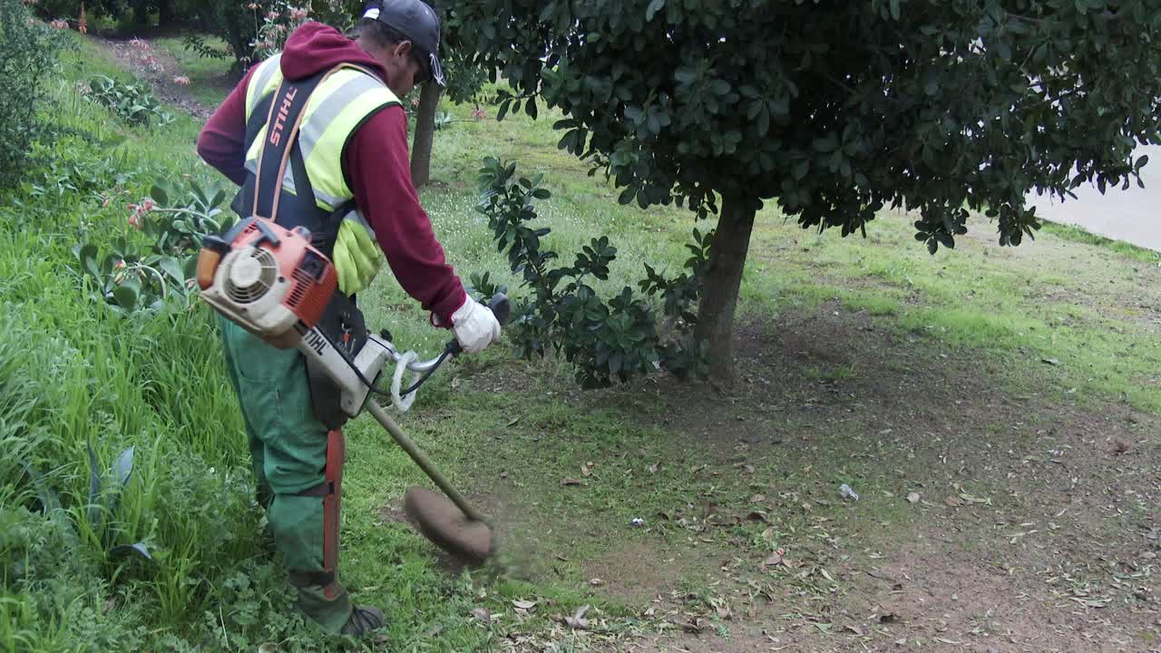 Council worker cutting grass and weeds on the road verge using a weed eater