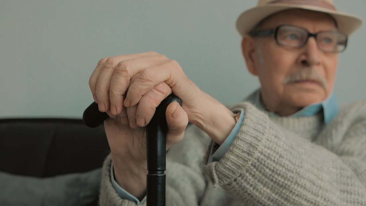 회색 콧수염, 모자, 안경, 지팡이를 가진 진지한 노인의 초상화