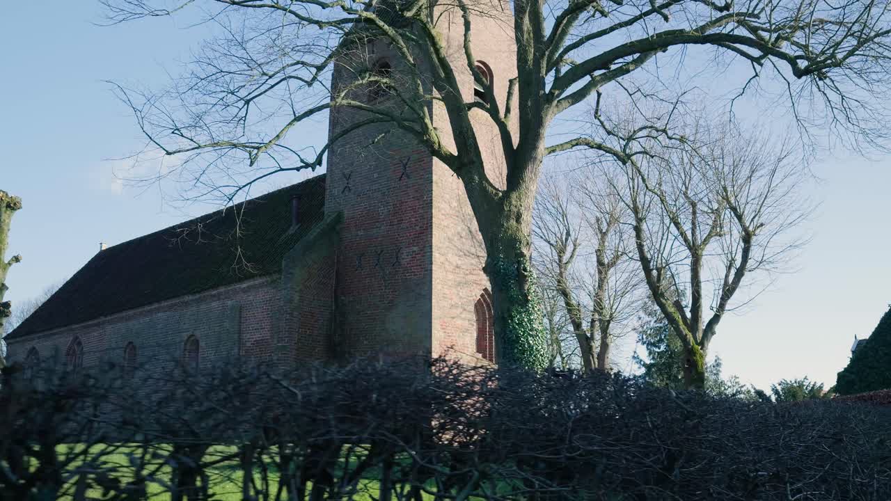 Antico campanile in mattoni e alberi spogli sotto il sole invernale.