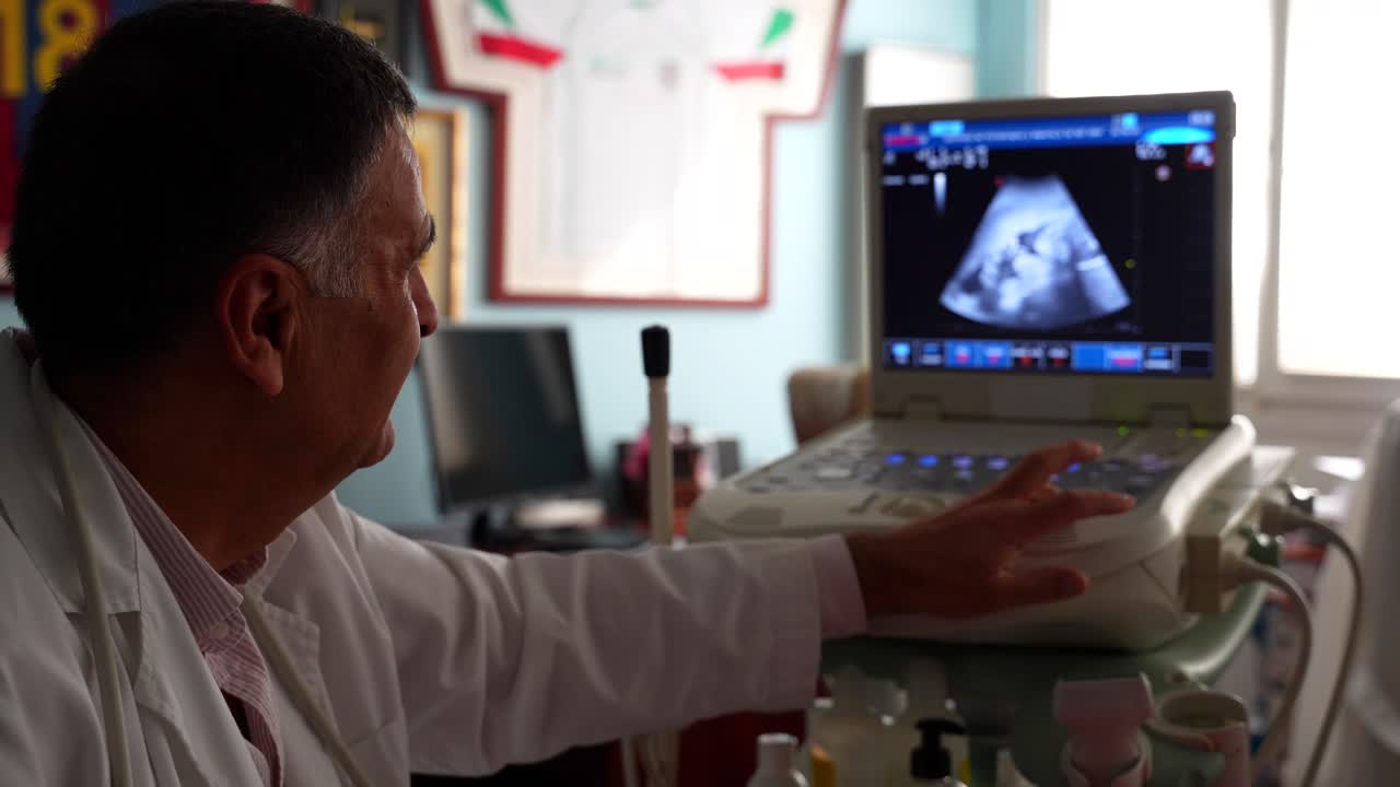 Primo piano di ginecologo che regola l'ecografo, ingrandisce, spiegando il bambino