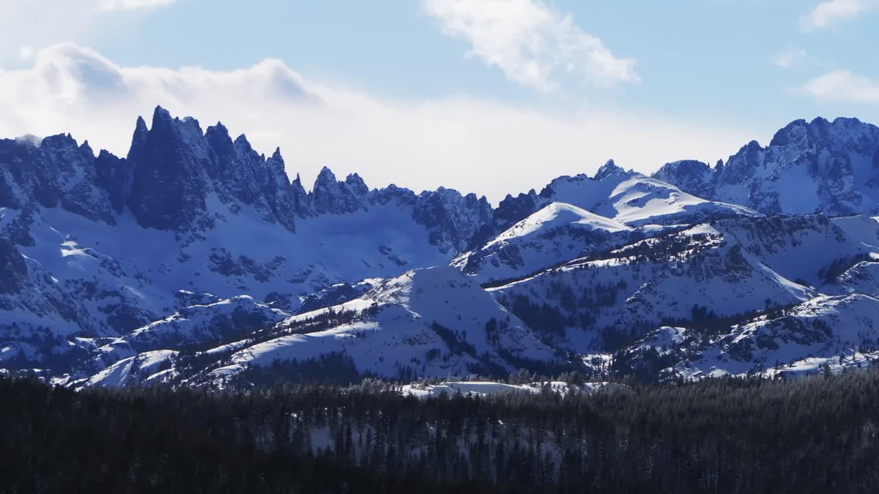 The Hemlocks Mammoth Mountain ski snowboard resort winter sunny blue sky afternoon aerial drone California The Minarets jagged towering peaks fresh deep snow clouds Inyo National Forest pan left
