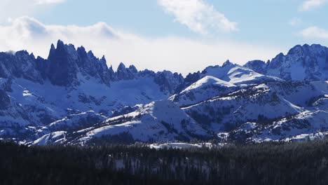 the hemlocks mammoth mountain ski snowboard resort winter sunny blue sky afternoon aerial drone california the minarets jagged towering peaks fresh deep snow clouds inyo national forest pan left