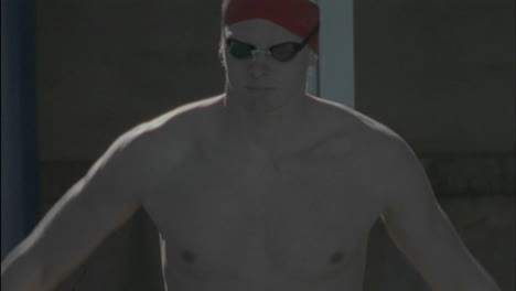 a male swimmer limbers up then dives into the pool