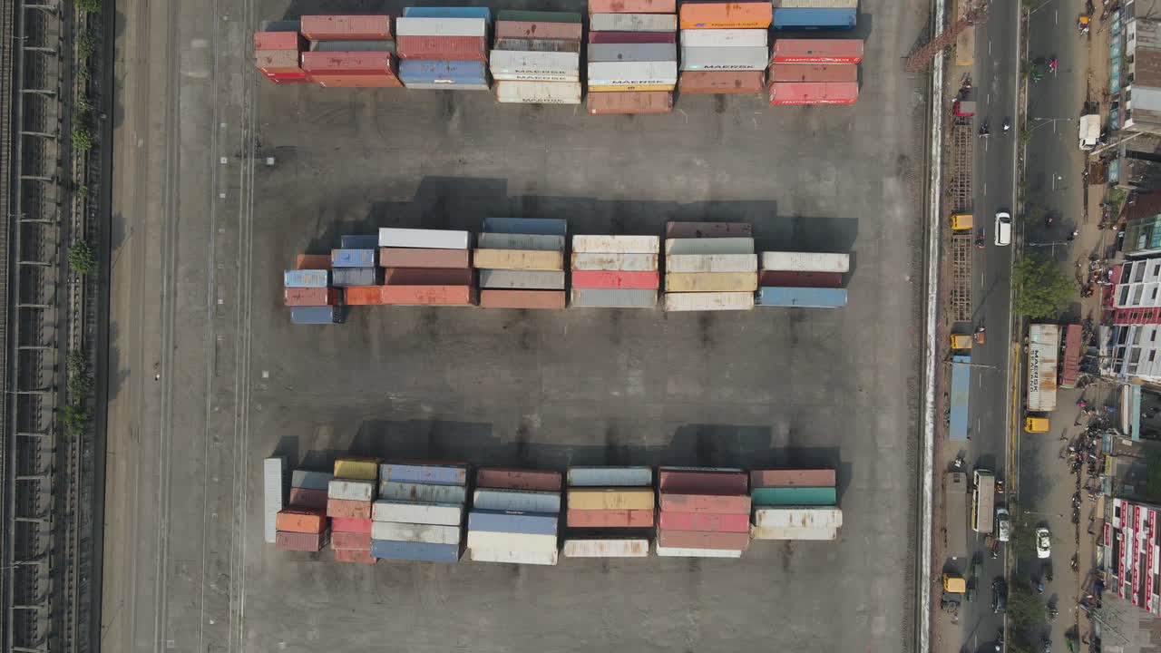 Top down aerial inland shipping container depot beside urban city road - drone flight ascending shot