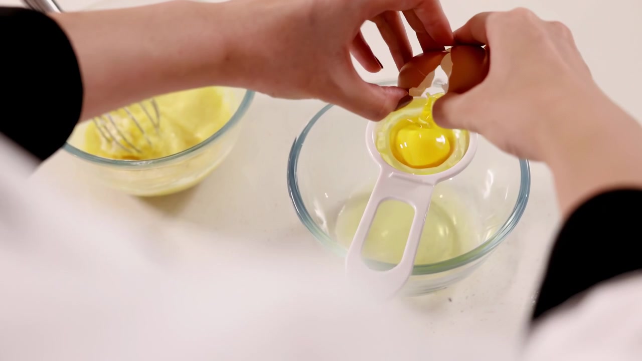Pastry chef baker using an egg separator tool to remove separate egg yolk from the white over white bowl for delicious birthday bakery order, ideal for cooking baking, confectionery, culinary