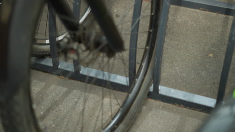 close-up of bicycle wheel and metal bike rack in urban setting, capturing details of wheel spokes and parking stand, other bicycle wheels visible in background