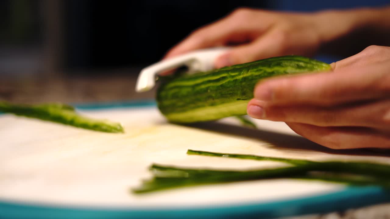 Slowly peeling healthy cucumber with vegetable scraper in home kitchen, close-up