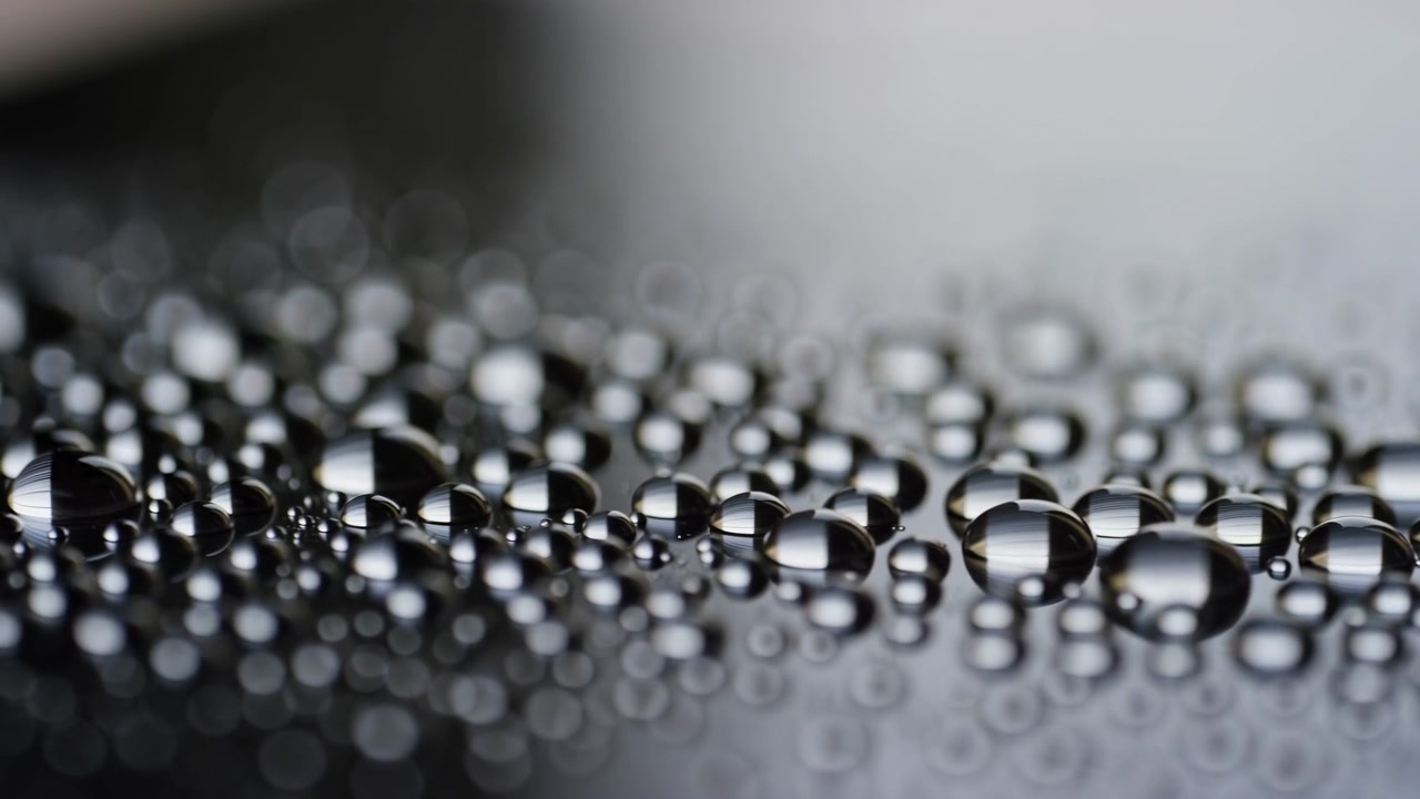 Punto temporale macro che mostra goccioline d'acqua immobili su una superficie scura riflettente a metà di un breve