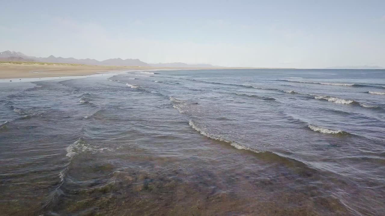 vuelo bajo sobre una playa rocosa y el océano bajo el sol durante el verano soleado en la península de snaefellsness, islandia