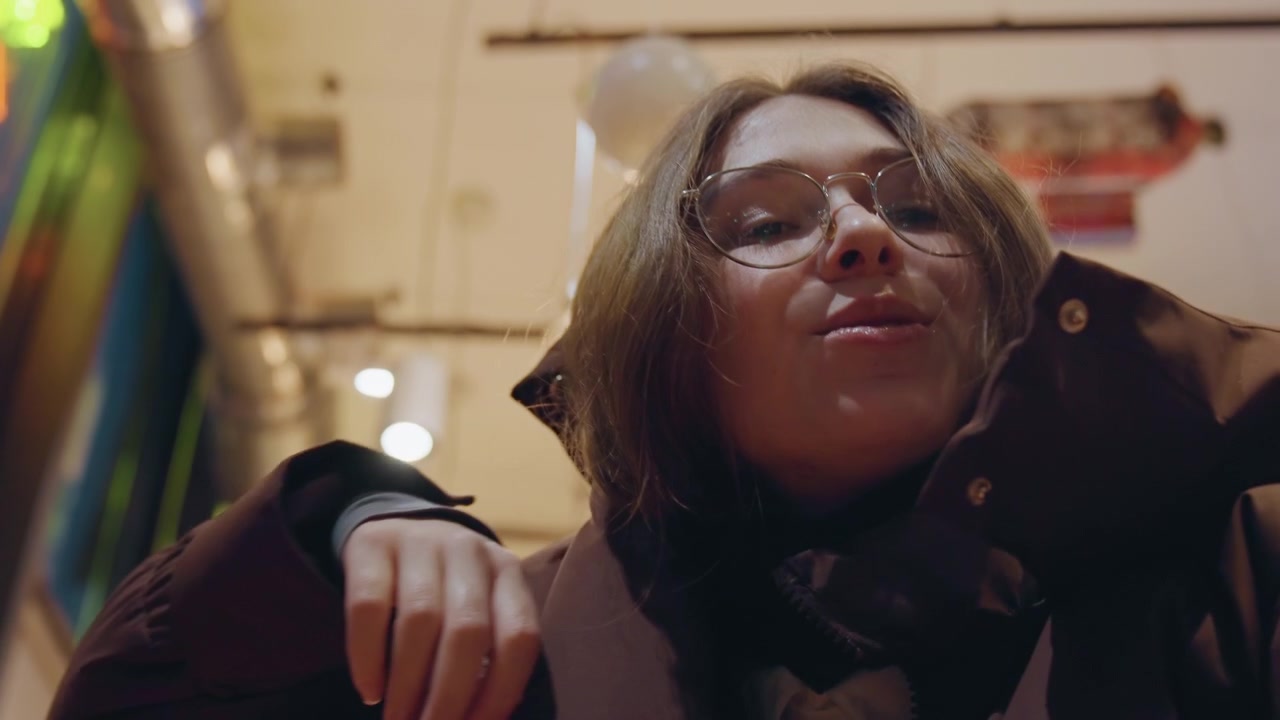 White woman putting on coat, brown puffer jacket and scarf, hands zipping hood in warm cafe light, preparing to step outside into chilly evening, candid commuter and boutique shopper vibes, cinematic