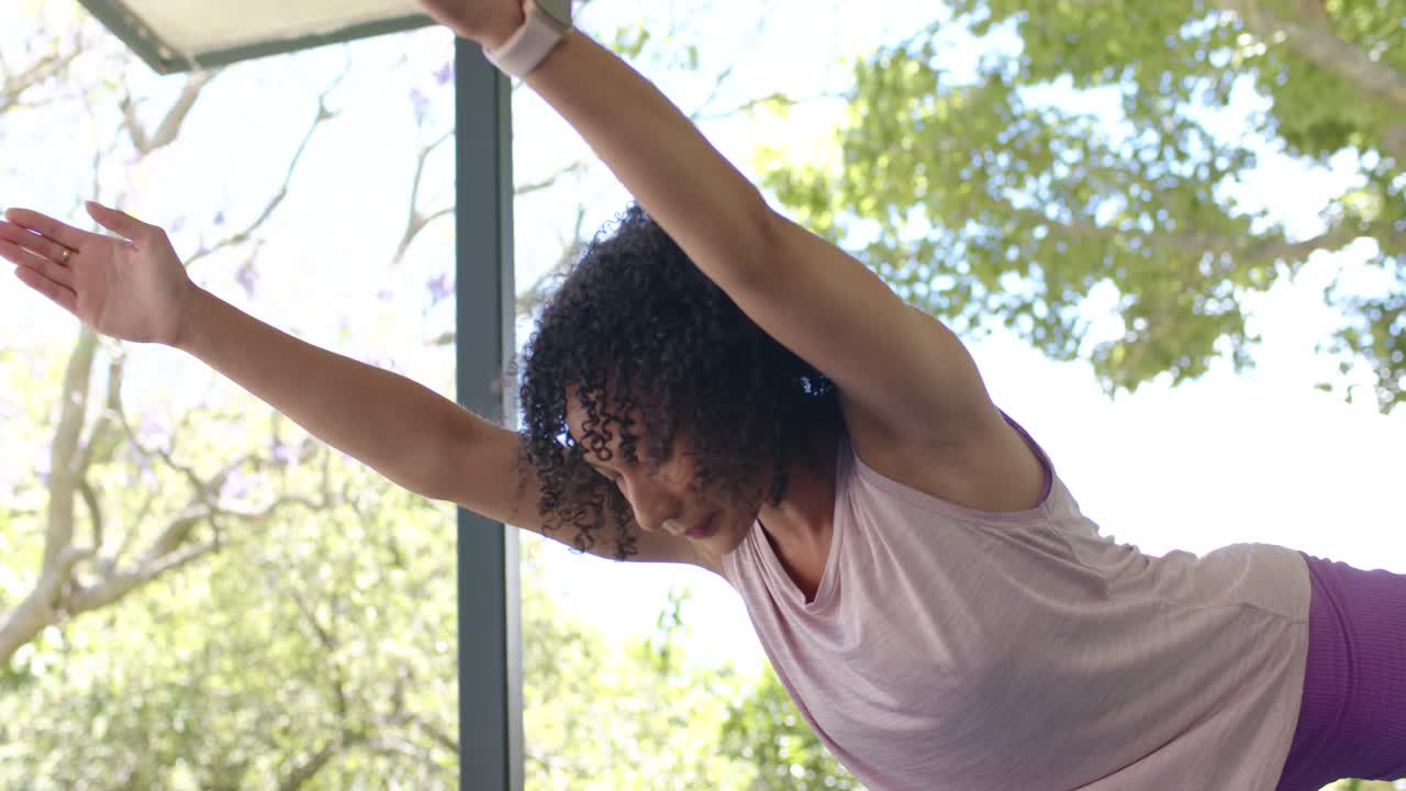 Woman is starting on one leg in glass patio, reaching forward, lifting back leg, practicing balance