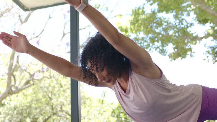 Woman is starting on one leg in glass patio, reaching forward, lifting back leg, practicing balance