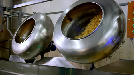 two metal rotating tanks filled with sweet snacks. corn sticks being covered with sugar syrup from a special disperse device.