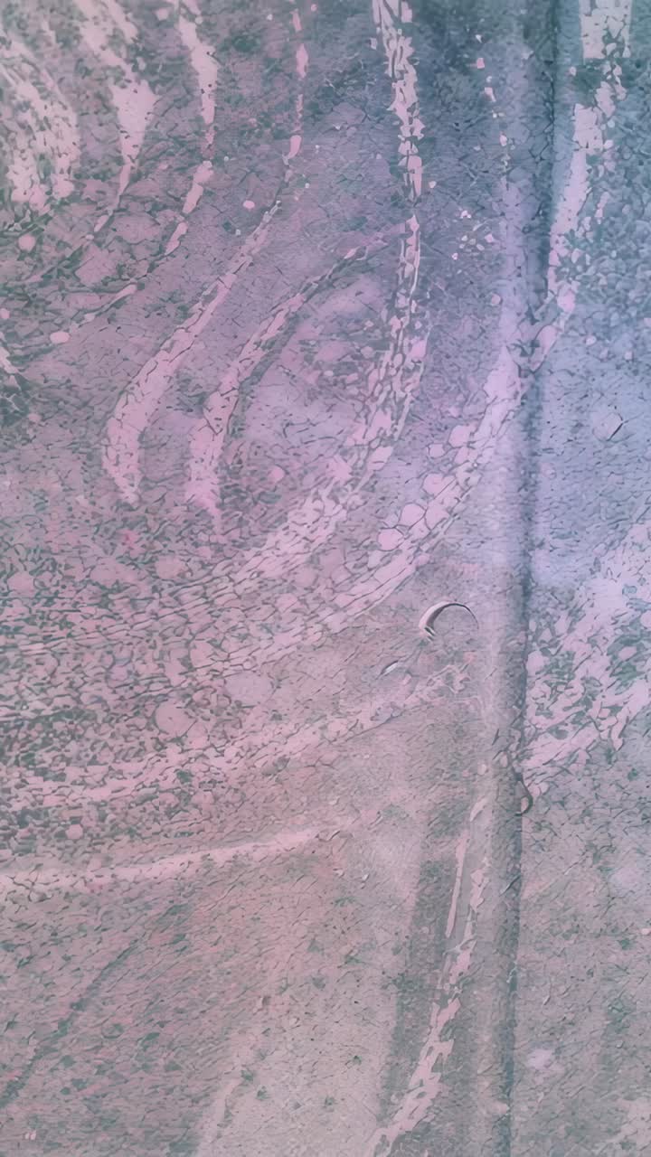 Vertical video: Shifting swirl residue and droplets moving on glass panel seam, from light shift