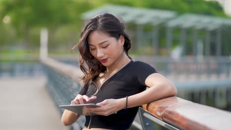 Attraktive,-Selbstbewusste,-Fitte-Frau-In-Sportbekleidung,-Läuferin-Spielt-Tablet-Computer-Und-Checkt-Soziale-Medien-Auf-Dem-Mobiltelefon-In-Der-Natur-Steht-Für-Einen-Gesunden-Lebensstil