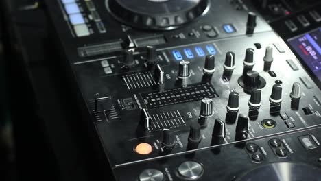 Camera tilting shot on DJ equipment with headphone and speaker monitor at a table with black background inside studio room at night