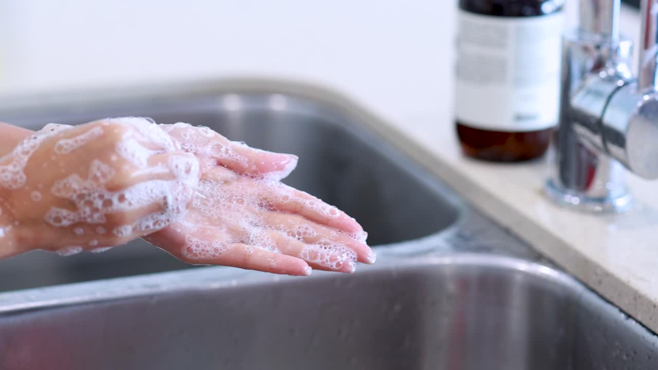 Hands are carefully washed with soap under running water in a bright kitchen setting. Close-up shots highlight proper hygiene technique and foamy lather