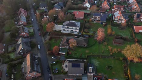 dusk scene in modern neighborhood of usa. large garden and houses with solar panels on roof. red brick style homes in germany at sunset. aerial top down flyover.