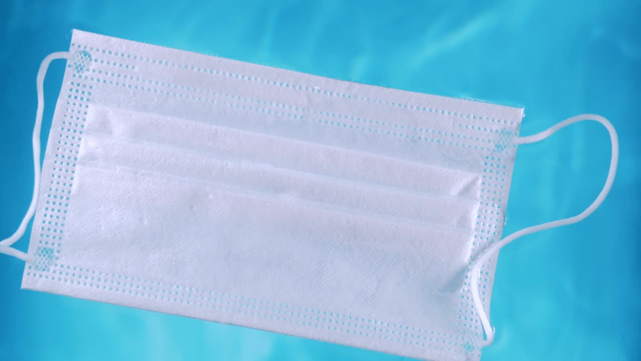 una máscara protectora médica en la superficie del agua contaminación del agua durante la crisis del covid-19 con lazos que se desplaza lentamente en la superficie del agua