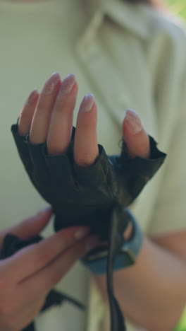 primer plano de exteriores individuales quitando cuidadosamente el guante de motociclista de la mano izquierda con luz solar natural destacando los movimientos de la mano, en un telón de fondo de vegetación exuberante borrosa