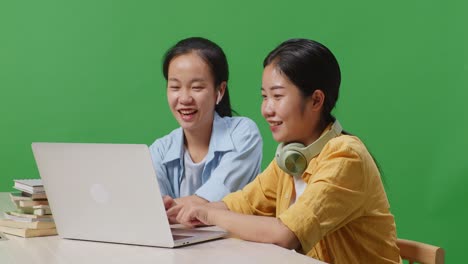 close up of asian woman student teaching her friend on a laptop while sitting on a table in the green screen background classroom