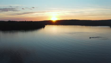 drone shot over a beautiful sunset on a lake with a single boat waterskier in quebec, canada