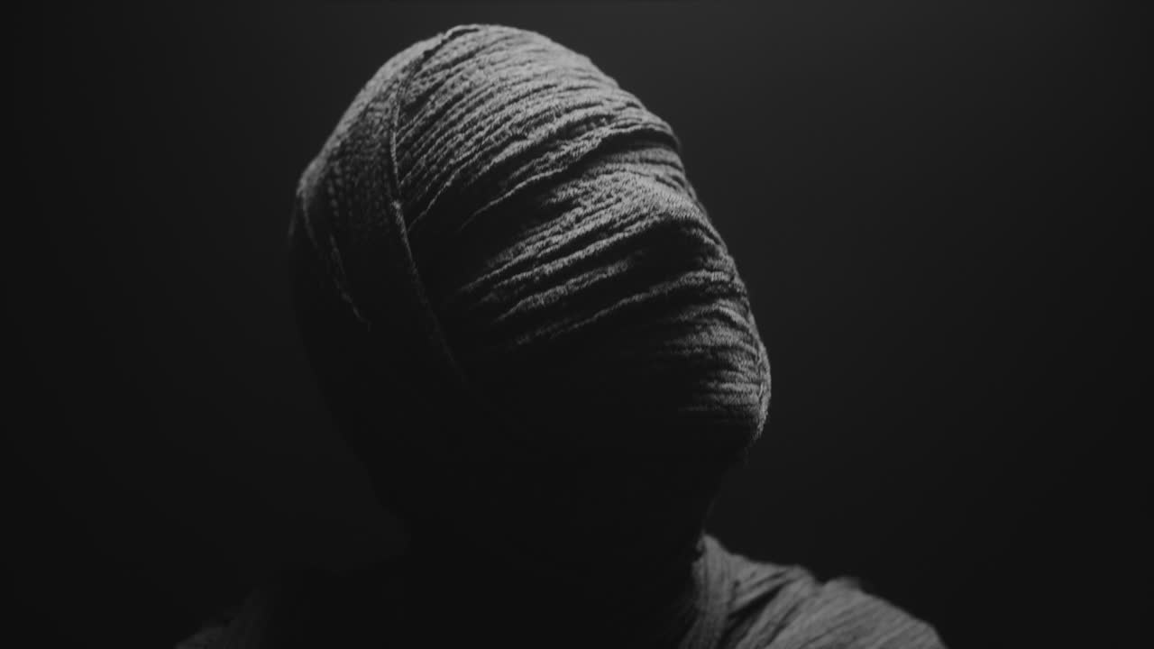 A mummy of a woman on a dark backdrop rises  and then turns her head