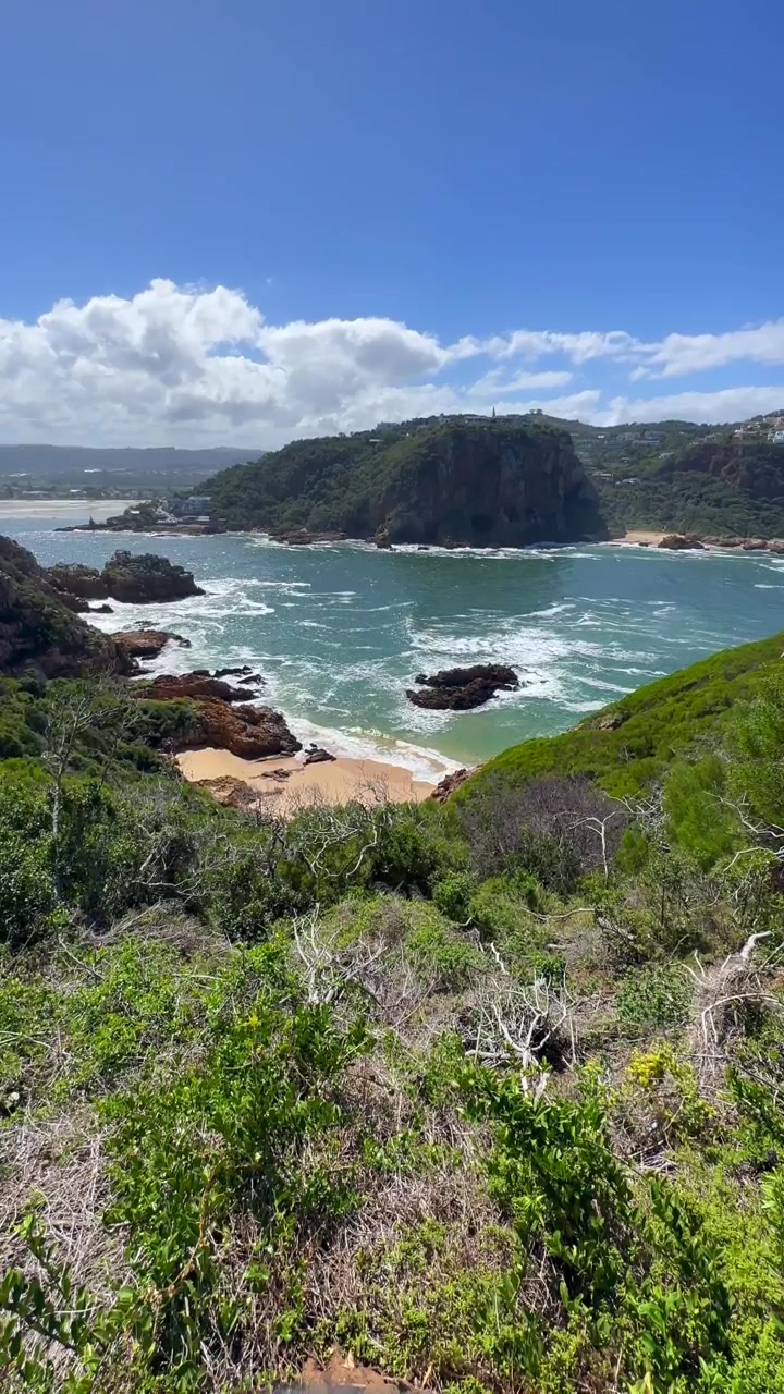 Le onde si infrangono contro scogliere rocciose a Knysna, Sudafrica, sotto un cielo azzurro e limpido